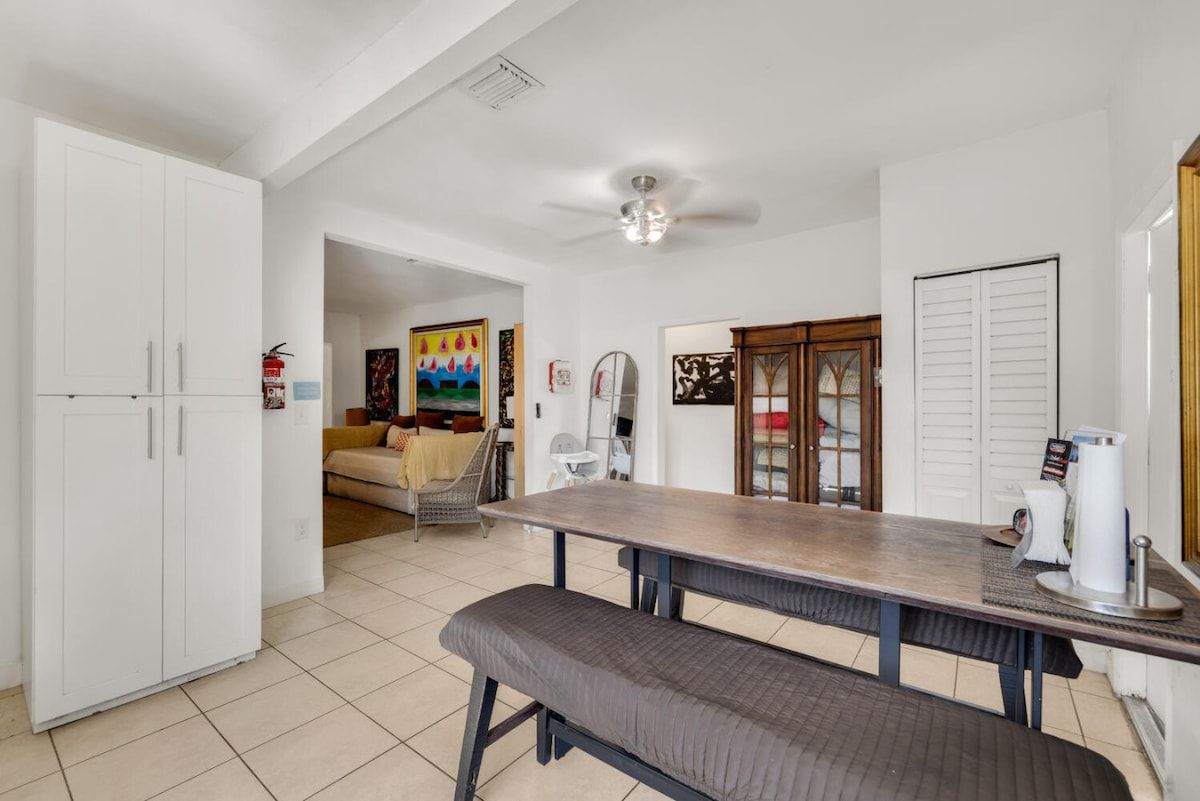 A kitchen with a dining table, bench, white cabinets, and a ceiling fan.