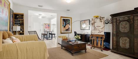 A living room with a sofa, a coffee table, and a cabinet. There is a painting on the wall and a lamp on a side table.