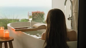 A person relaxing in a bathtub with a view of the ocean. - Couples Luxury Retreat with Ocean Views and Outdoor Bath (Penguin)