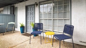 Un espace patio avec deux chaises bleues et une table jaune, une plante en pot et une porte portant le numéro 101.