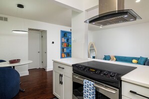 A modern kitchen with a built-in oven and stovetop, a white countertop, and a blue bookshelf. - Private Patio + Community Pool - First-Floor Condo (Dallas)