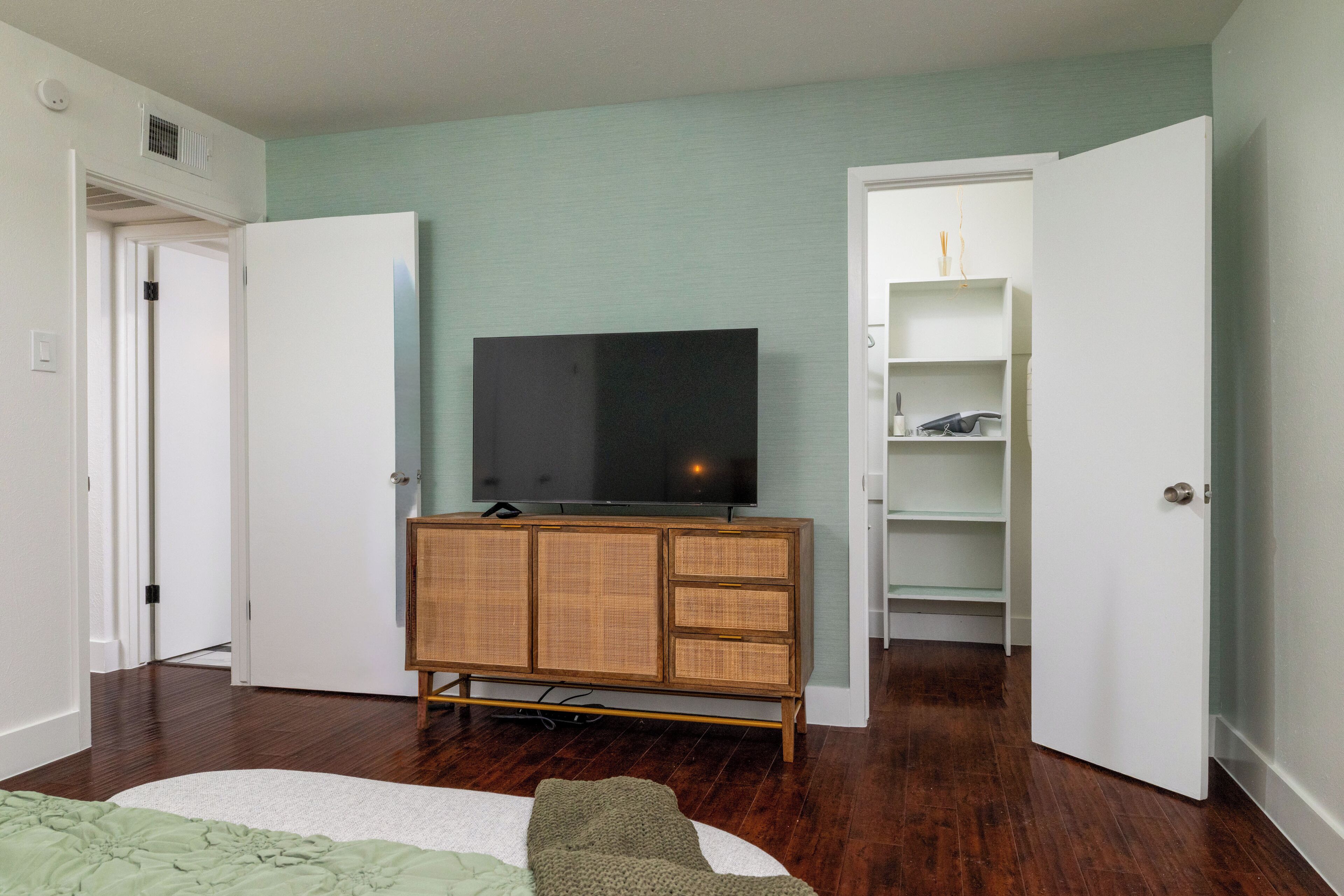 A room with a television on a wooden cabinet, a white door, and a white closet with shelves.