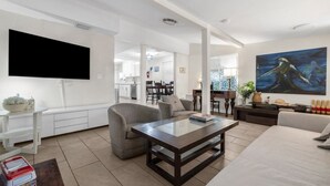 Un salon moderne avec un téléviseur à écran plat, un grand tableau et un coin repas à l’arrière-plan.
