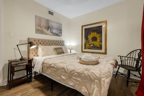 Une chambre à coucher avec un lit, des tables de chevet, une lampe, une chaise et deux tableaux encadrés accrochés au mur.