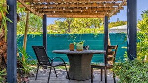 Une terrasse extérieure avec une table ronde et des chaises, entourée de verdure et d’une pergola en bois.