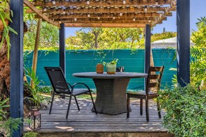 An outdoor patio with a round table and chairs, surrounded by greenery and a wooden pergola. - Artful Home Near Design District (Miami)