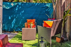 Un área de estar al aire libre con muebles de mimbre y cojines, una pequeña mesa con un florero y un farol.