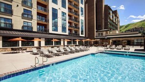 Ein Hotelpoolbereich mit Liegestühlen und Sonnenschirmen, umgeben von mehrstöckigen Gebäuden mit Balkonen.