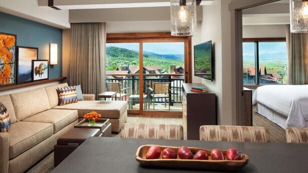 Ein Hotelzimmer mit einer Couch, einem Esstisch und einem Balkon mit schöner Aussicht.