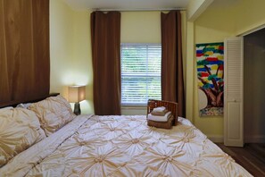 Un dormitorio con una cama grande, una mesita de noche, una lámpara, una ventana con persianas y un cuadro en la pared.