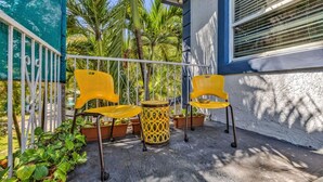 A balcony with two yellow chairs and a small round table, surrounded by potted plants and a metal railing. - Suarez Art Stay, 3BR Miami Oasis with Parking (Miami)