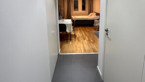 A narrow hallway leading to a bedroom with a bed, a small table, and a chair. - Stay Sollentuna (Sollentuna)