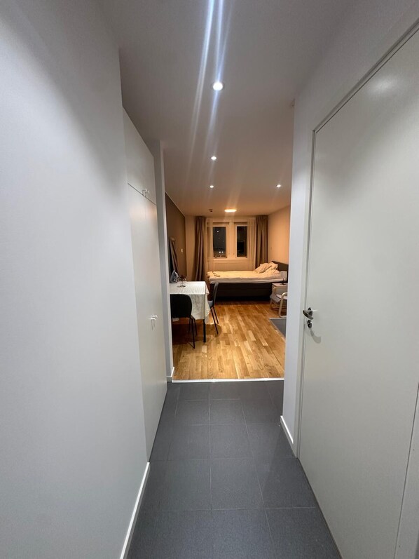 Un couloir étroit mène à une chambre qui contient un lit, une petite table et une chaise.