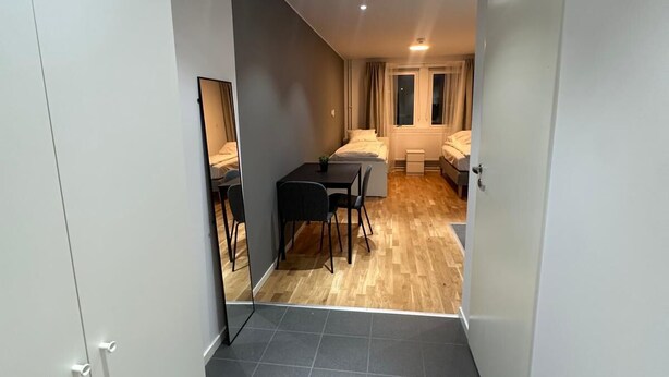 A modern hotel room with a dark tiled floor, a small dining area with a table and chairs, a bed with a window, and a wardrobe. - Stay Sollentuna (Sollentuna)