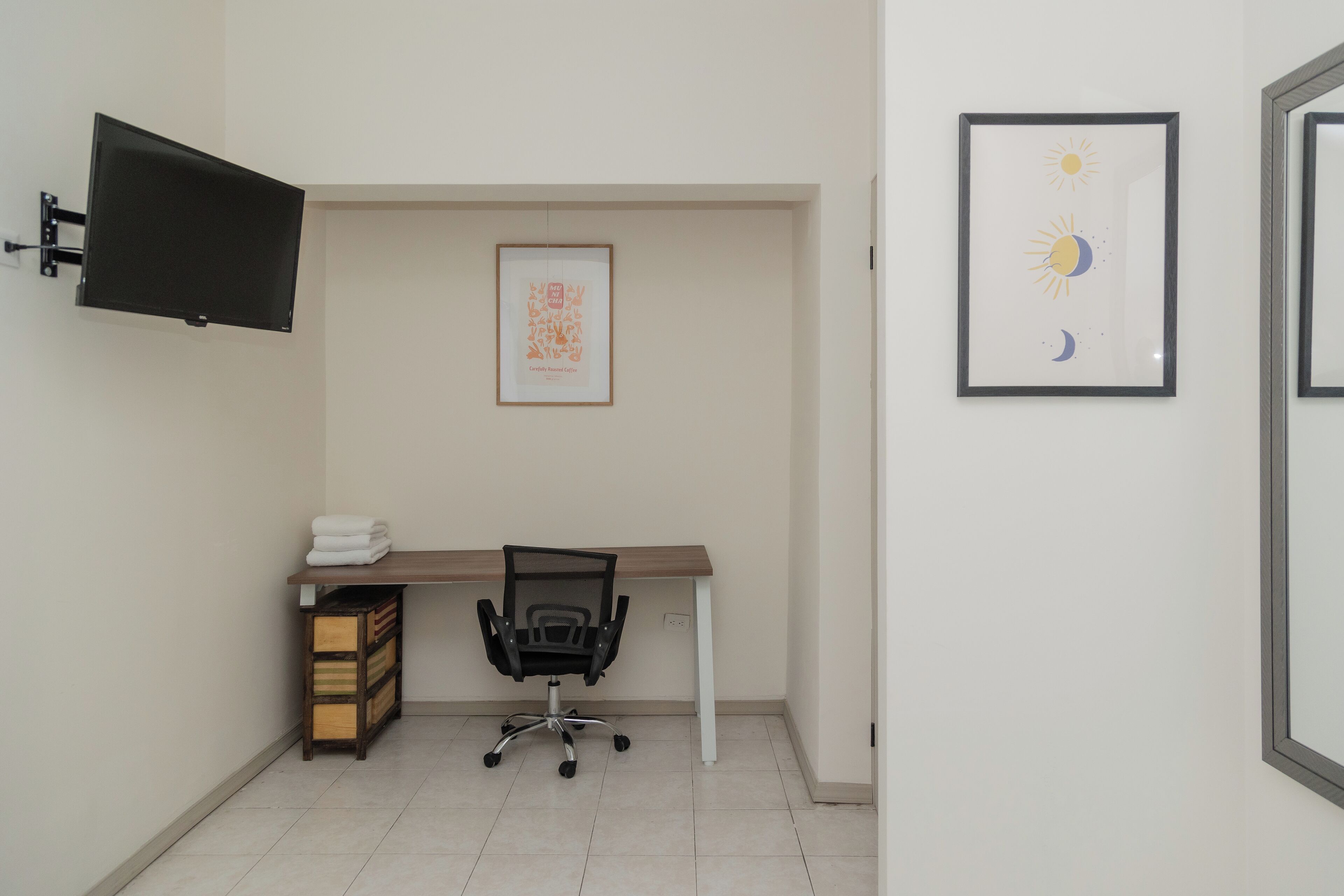 A small office with a desk, chair, and a mounted TV. There are framed pictures on the wall.
