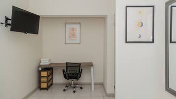 A small office with a desk, chair, and a mounted TV. There are framed pictures on the wall.