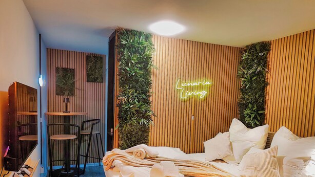 Una camera da letto moderna con un letto, un neon, un piccolo angolo salotto e una parete con listelli di legno verticali.