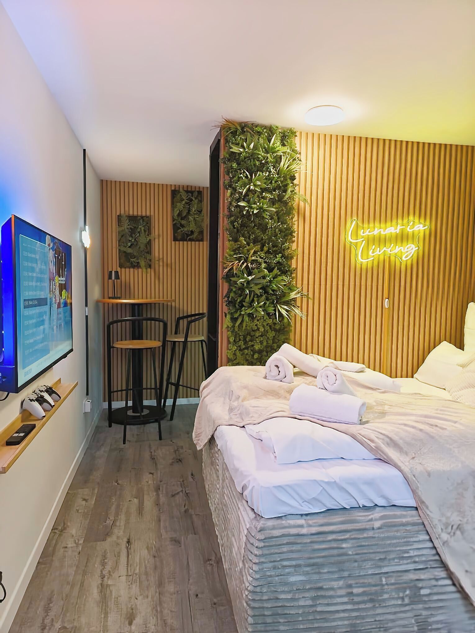 Moderni hotellihuone, jossa on sänky, työpöytä ja tuoli. Seinällä on neonvalomainos ja toisella seinällä televisio.