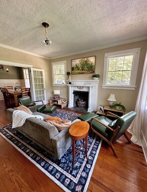 A living room with a fireplace, green leather chairs, a sofa, and a patterned rug. - Charming cottage near the Wilcox & Historic Downtown. 4 Bedrooms (Aiken)