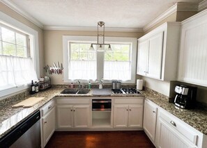 A kitchen with white cabinets, a granite countertop, a stove, a sink, and a window with curtains. - Charming cottage near the Wilcox & Historic Downtown. 4 Bedrooms (Aiken)
