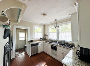 Une cuisine avec des meubles blancs, un plan de travail en granit, un lave-vaisselle, une cuisinière et une fenêtre donnant sur un paysage verdoyant.