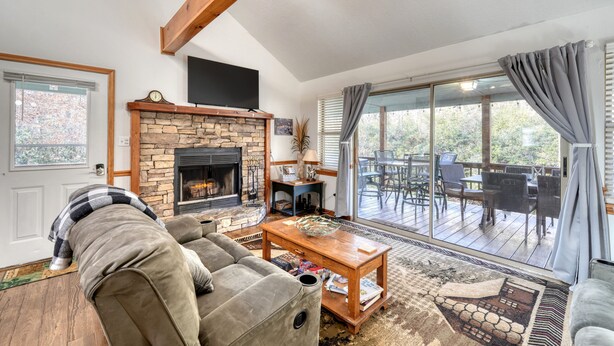 A cozy living room with a stone fireplace, a comfortable sofa, a coffee table, and a view of the outdoor deck through large sliding glass doors. - Steps to Shooting Creek (Hayesville)