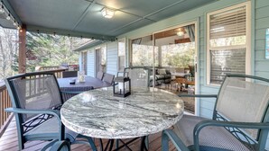 A covered outdoor patio with a round table and chairs, a lantern, and a view of the interior through glass doors. - Steps to Shooting Creek (Hayesville)