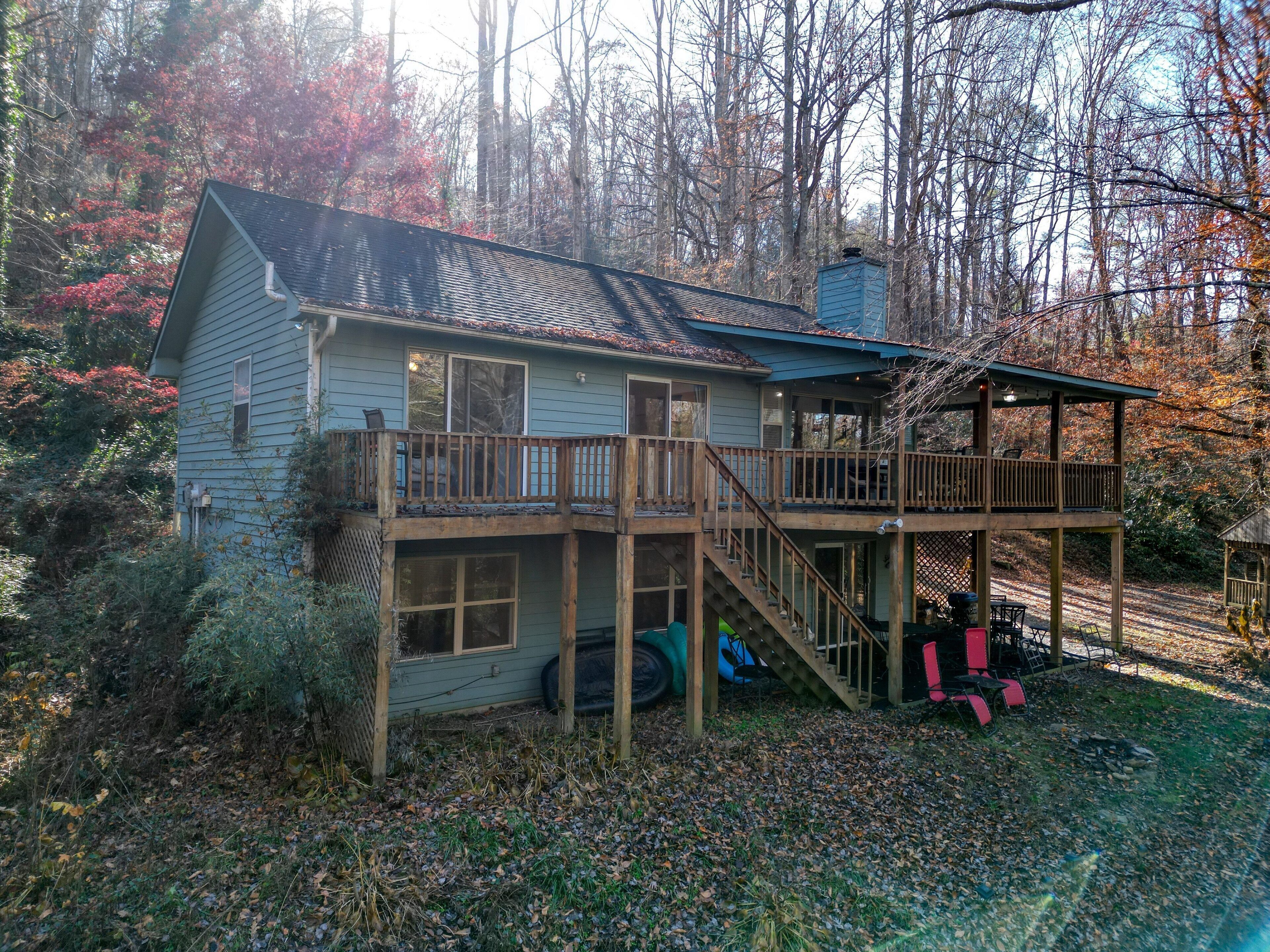 A two-story cabin with a deck and stairs, surrounded by trees and a forested area.