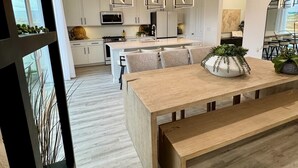 A modern kitchen with white cabinets, a central island, pendant lights, and a dining area with a wooden table and bench. - Magical Mountain-View Retreat SwimSpa-Hot Tub , Fire pit & Cozy Living Spaces  (Salem)