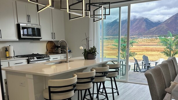 A modern kitchen with a central island, bar stools, and a view of mountains through large windows. - Magical Mountain-View Retreat SwimSpa-Hot Tub , Fire pit & Cozy Living Spaces  (Salem)