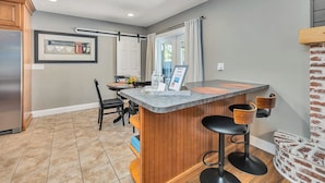 A kitchen with a bar area, wooden cabinets, a refrigerator, and a dining table with chairs.