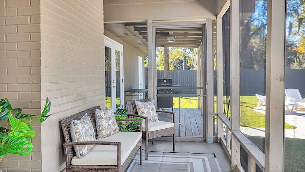 A covered patio with wicker furniture, a grill, and a view of a backyard.