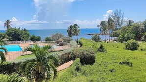 A resort with a swimming pool, lush greenery, and a view of the sea. - Studio Paradis Le Gosier - Sea view, close to beaches & restaurants (Le Gosier)