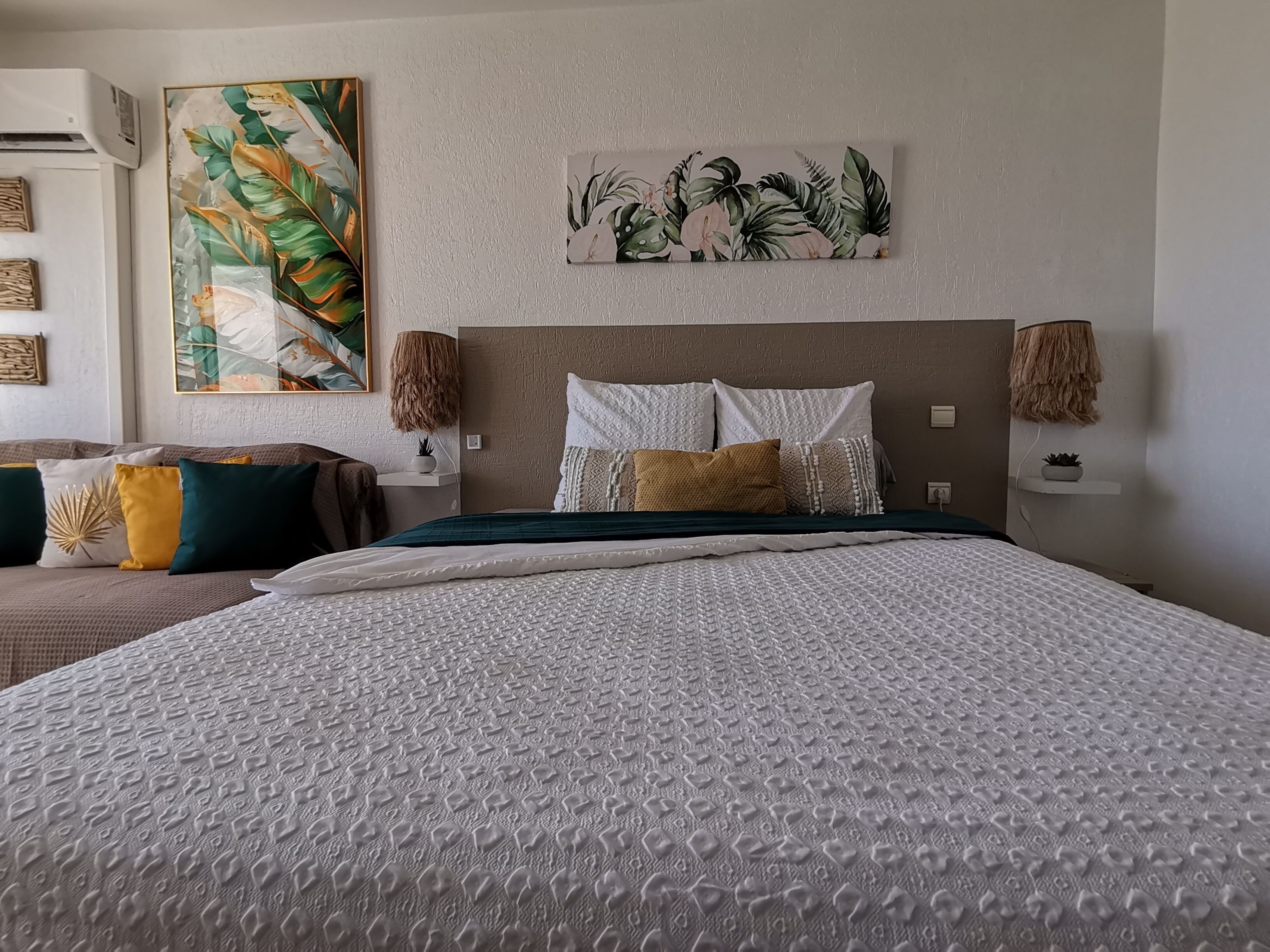 Ein modernes Schlafzimmer mit einem großen Bett, einem Kopfteil, Wandbildern und einem Nachttisch mit einer Lampe.