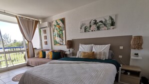 A spacious bedroom with a large bed, a balcony with curtains, and tropical-themed wall art. - Studio Paradis Le Gosier - Sea view, close to beaches & restaurants (Le Gosier)