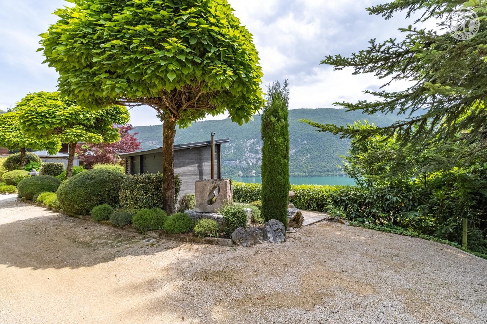 Un giardino curato con un vialetto sterrato, siepi ben potate e diversi alberi.