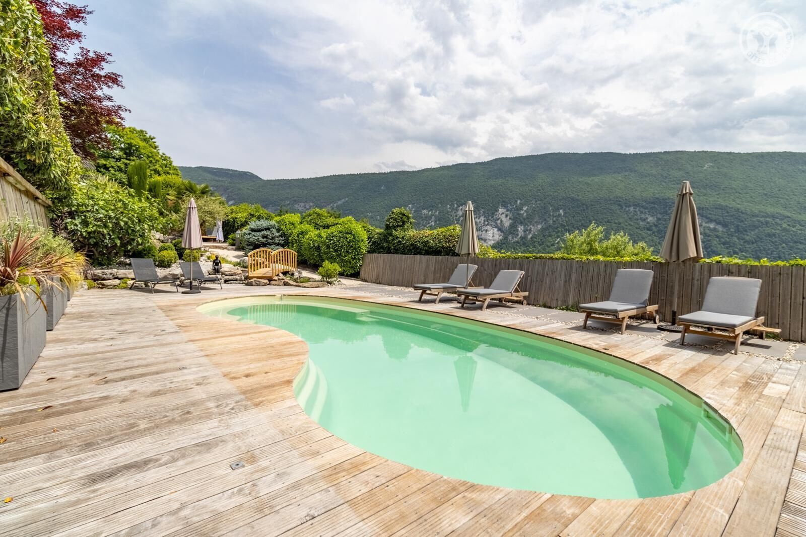 Um deck de madeira com piscina, cadeiras de sol e cerca de madeira.