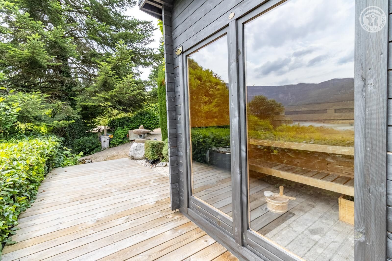 A wooden deck with a glass door leading to a garden area with a stone bench and a small table.