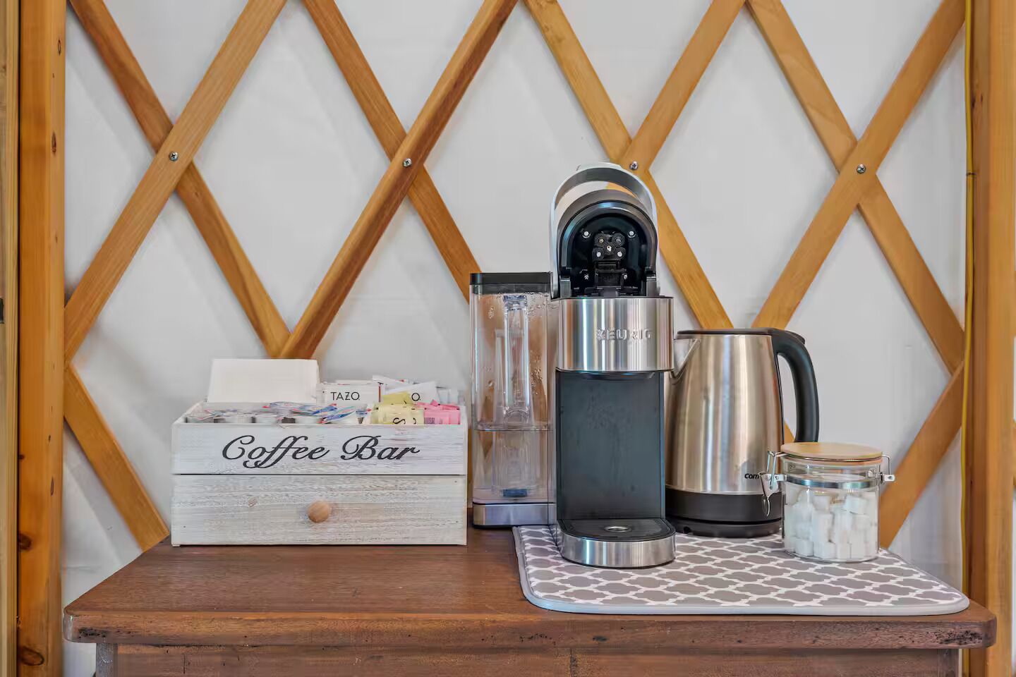 A coffee bar setup with a Keurig coffee maker, a coffee pot, a glass carafe, and a box labeled "Coffee Bar" containing coffee pods.