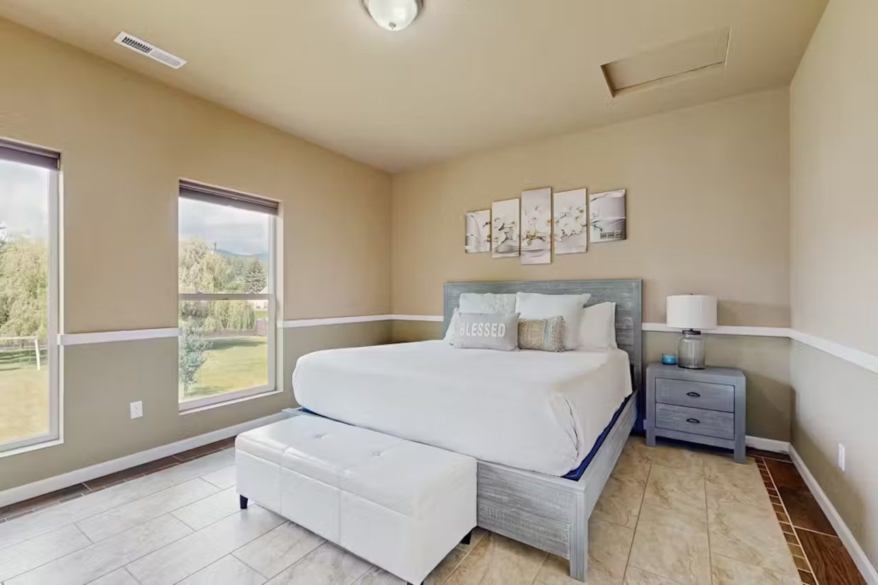 A bedroom with a large bed, a nightstand, and a window with a view of greenery.