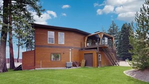 Una casa moderna de dos pisos con fachada de madera, un espacio exterior cubierto y un césped bien cuidado.