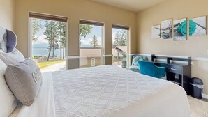 Una habitación de hotel con una cama grande, un escritorio y un balcón con vistas a árboles y al mar.