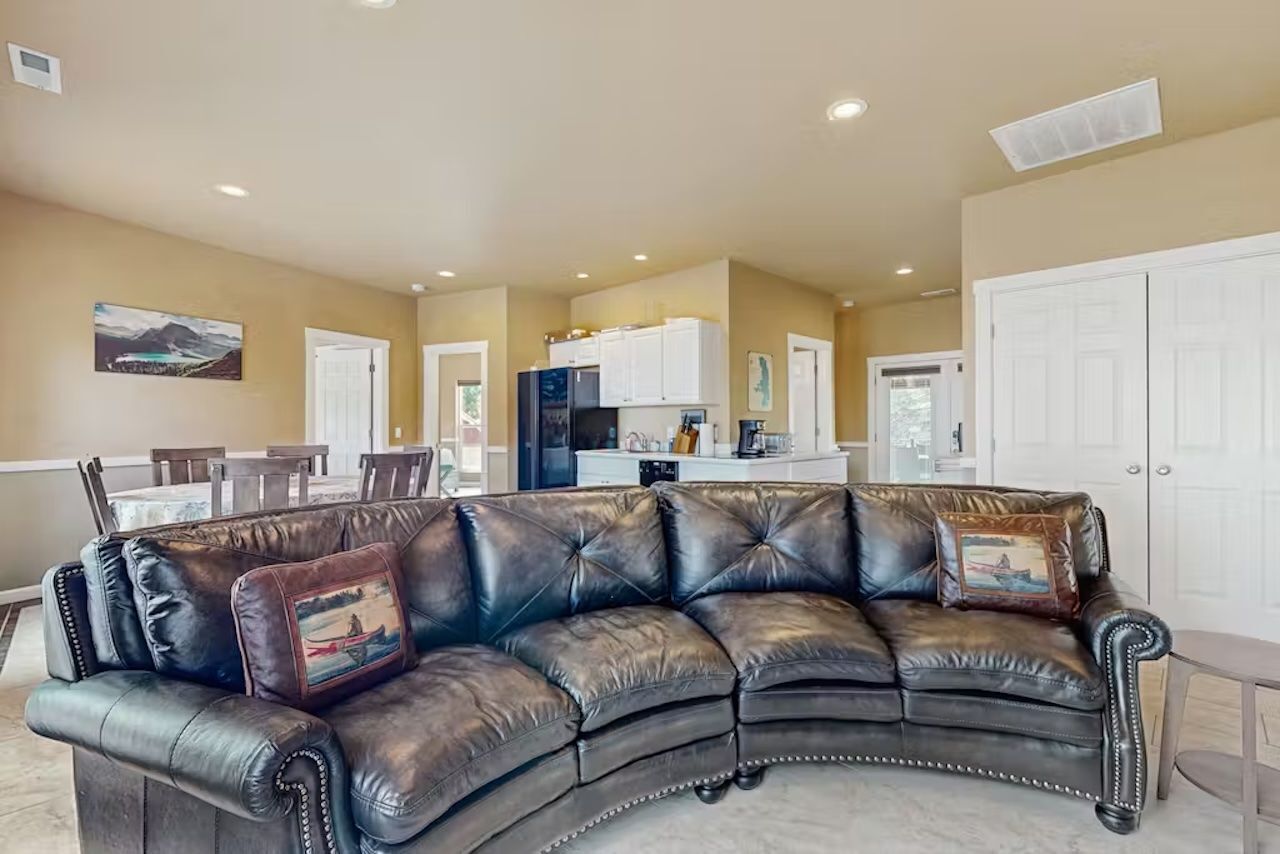 A living room with a leather sectional sofa, a dining area with a table and chairs, and a kitchen in the background.