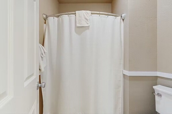 A bathroom with a white shower curtain, a towel rack with a towel, and a toilet.
