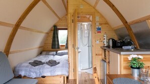 Een klein, houten interieur met een bed, kitchenette en douche.