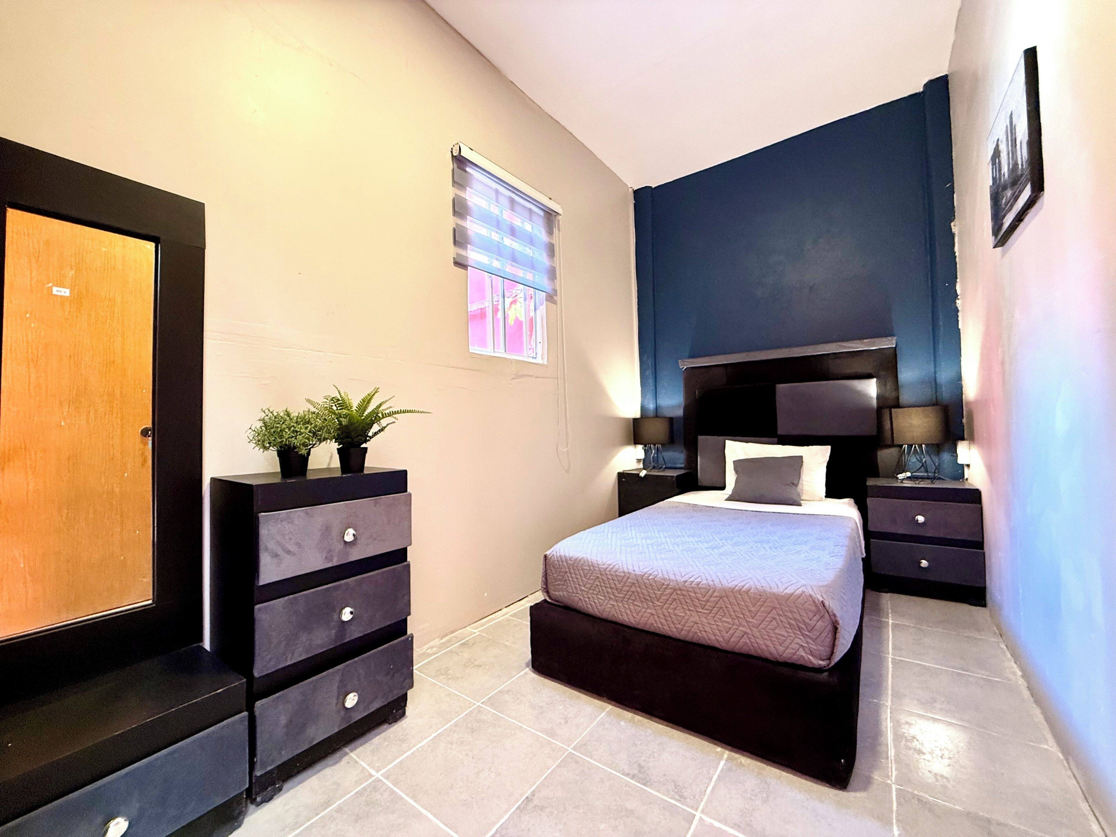 Un dormitorio con cama, cómoda, mesita de noche, ventana y puerta.