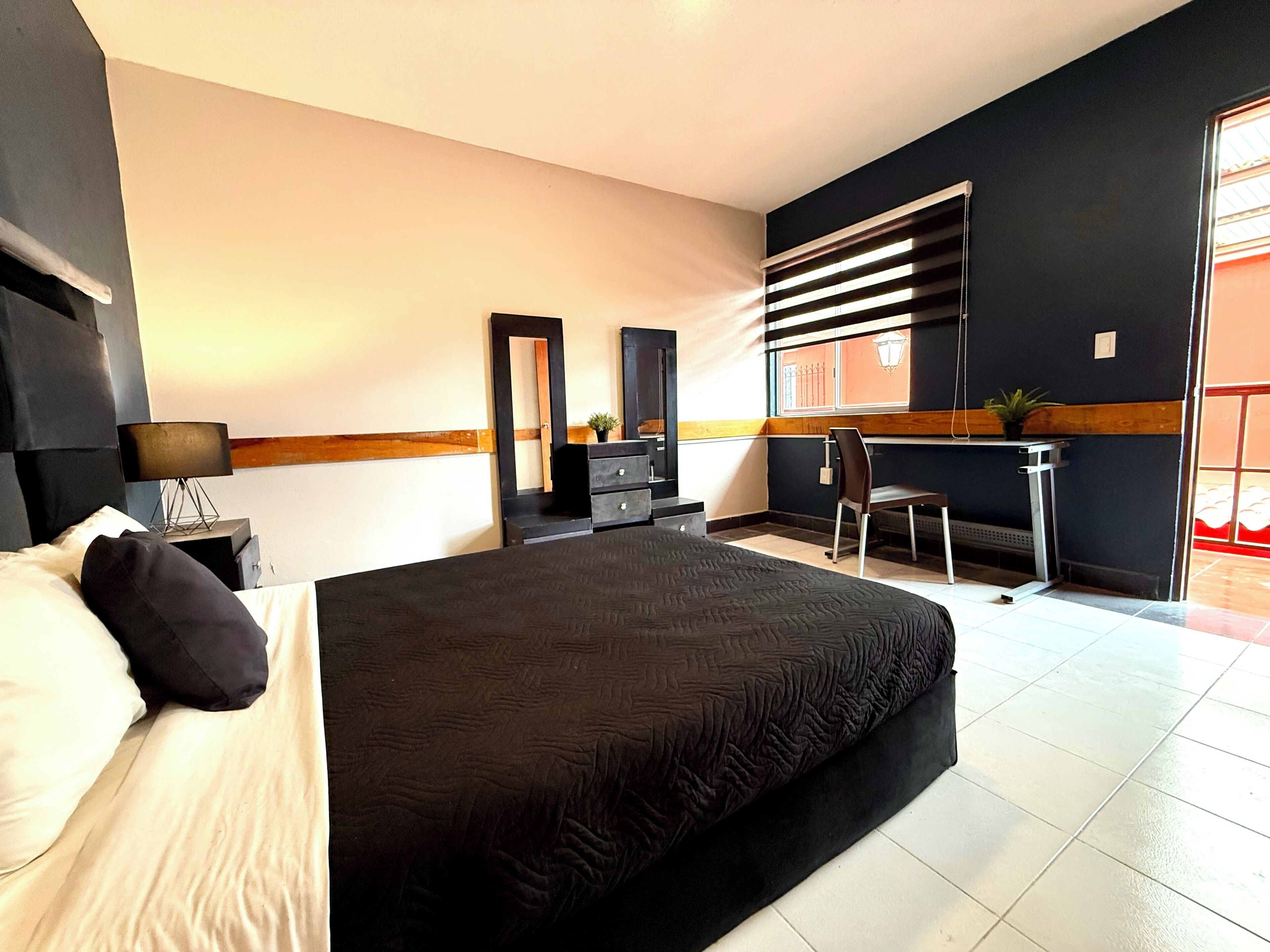 Ein Hotelzimmer mit einem großen Bett, einem Schreibtisch, einem Stuhl, einem Schminktisch und einem Spiegel.