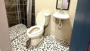 A bathroom with a tiled floor, a toilet, a sink, and a shower area. - RMS Hostal - Roma Norte (Mexico City)