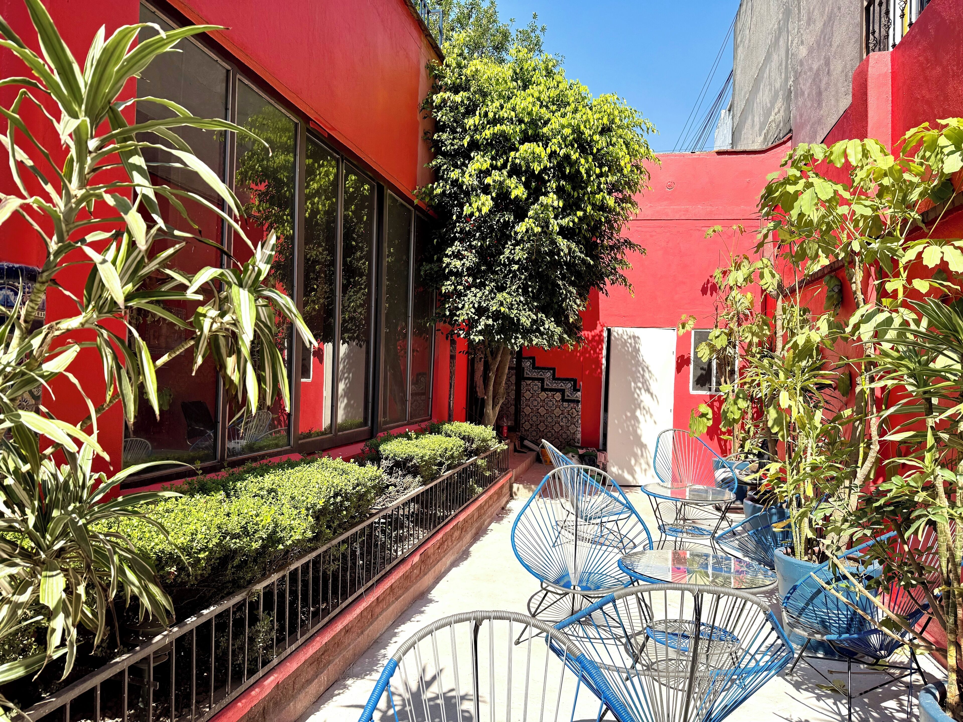 A red building with large windows, a metal fence, and blue chairs.
