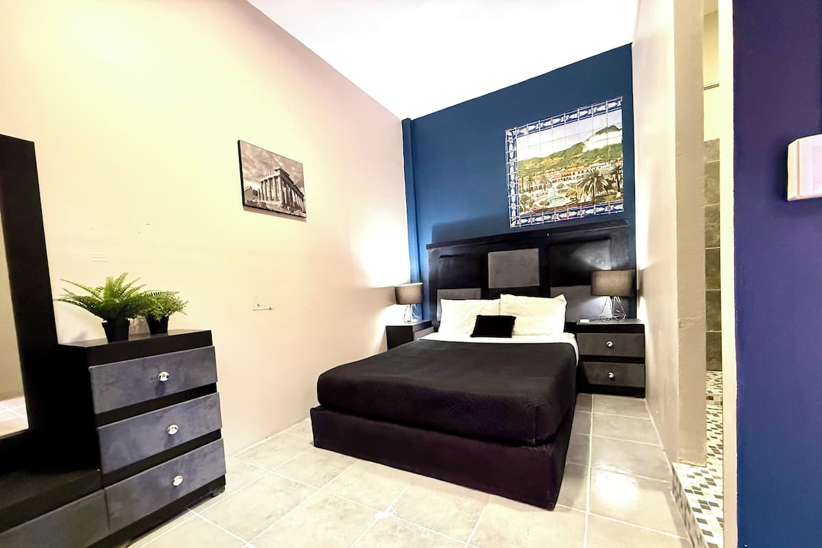 A modern bedroom with a bed, bedside tables, a dresser, and a decorative wall piece.